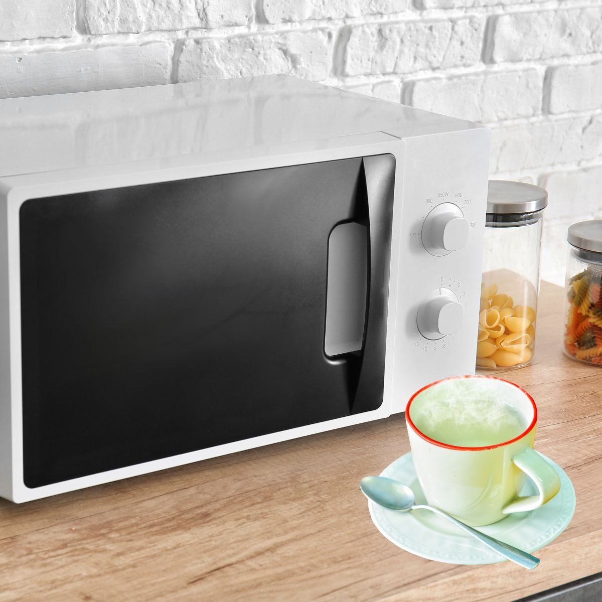A microwave with a cup of steaming water sitting in front of it.