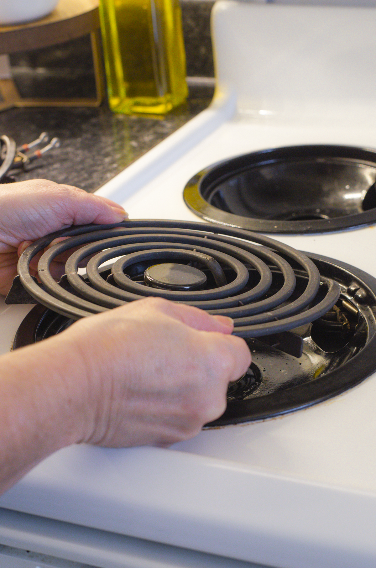 A woman removing the electric coil from a stovetop.