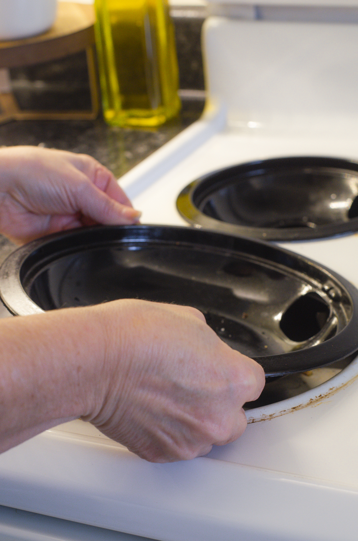 a woman removing the drip tray of an electric stovetop