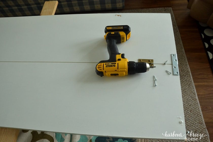 a bi fold closet door removed from the closet and laying flat on the floor. A straight metal piece is situated to be screwed to the top of where it is hinged.