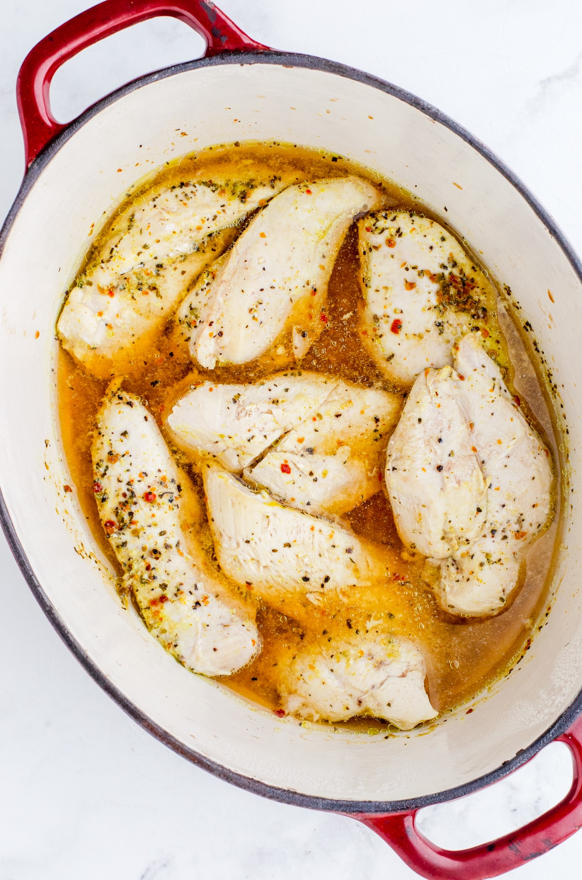 Cooked chicken breasts in a dutch oven with chicken broth.