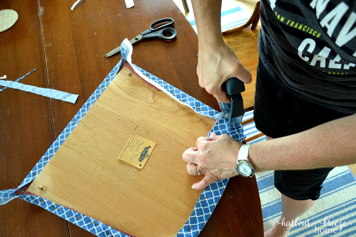 The corners of new fabric being stapled onto a dining chair cushion.