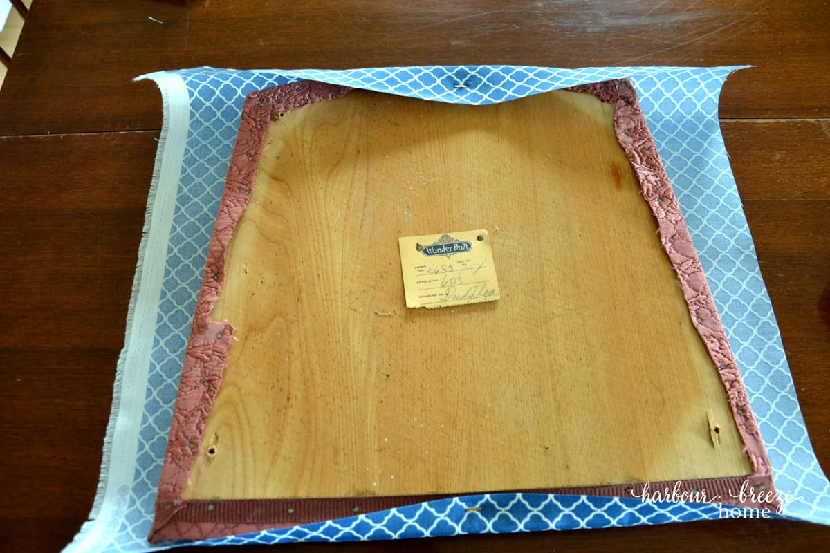 New fabric being stapled onto an old dining chair cushion.