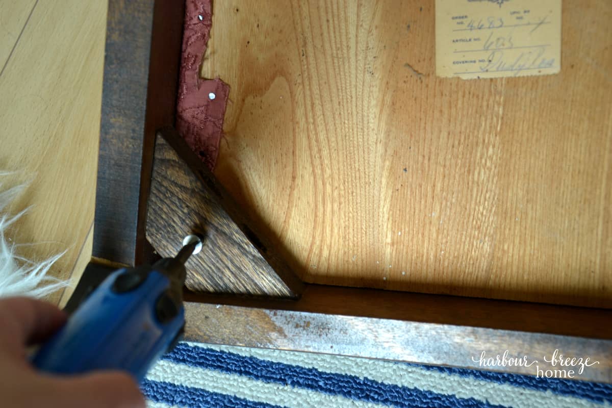 Unscrewing the chair cushion from the underside of a dining chair with a screwdriver.