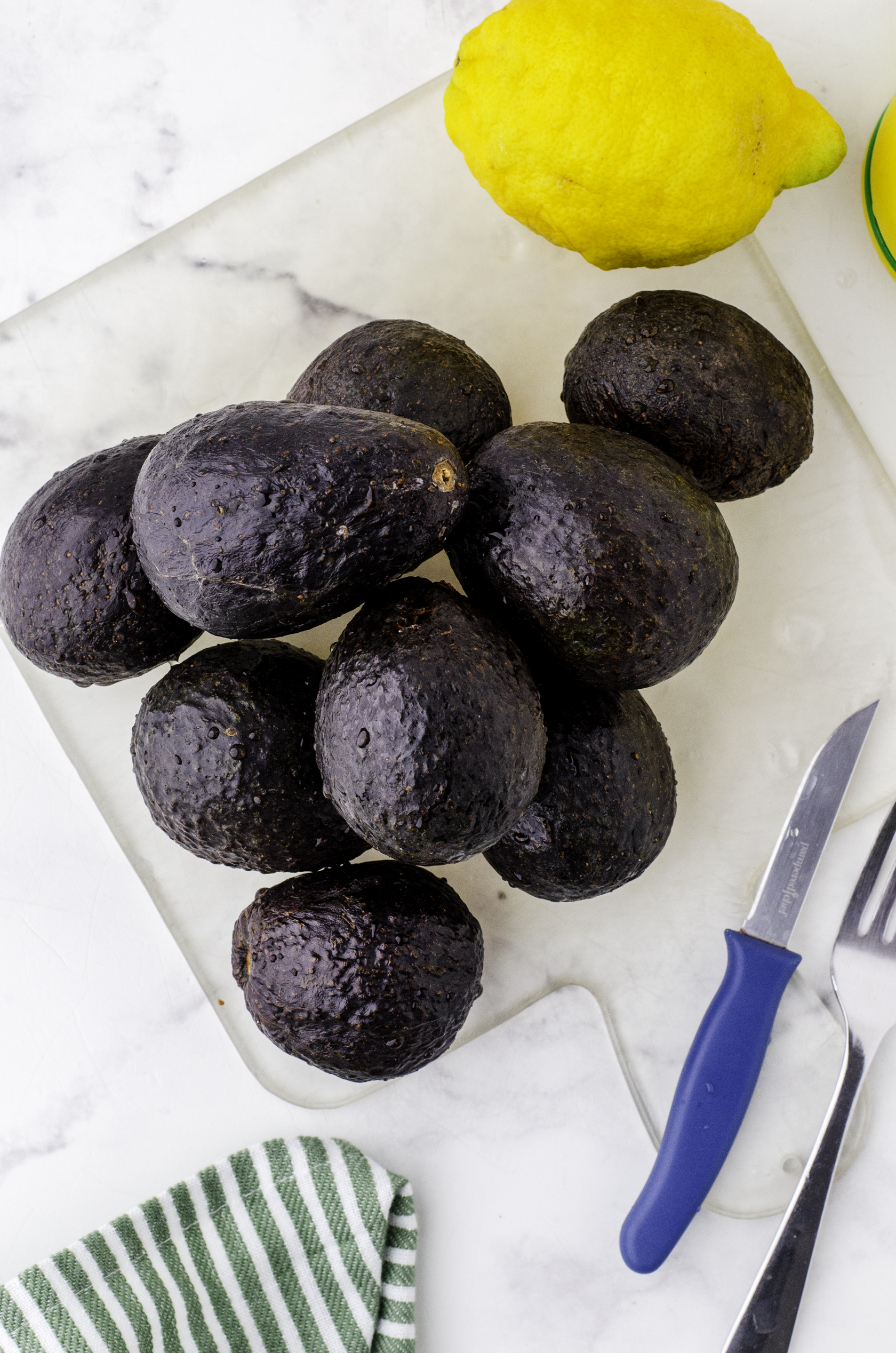 A pile of avocados and a lemon sitting on a cutting board.