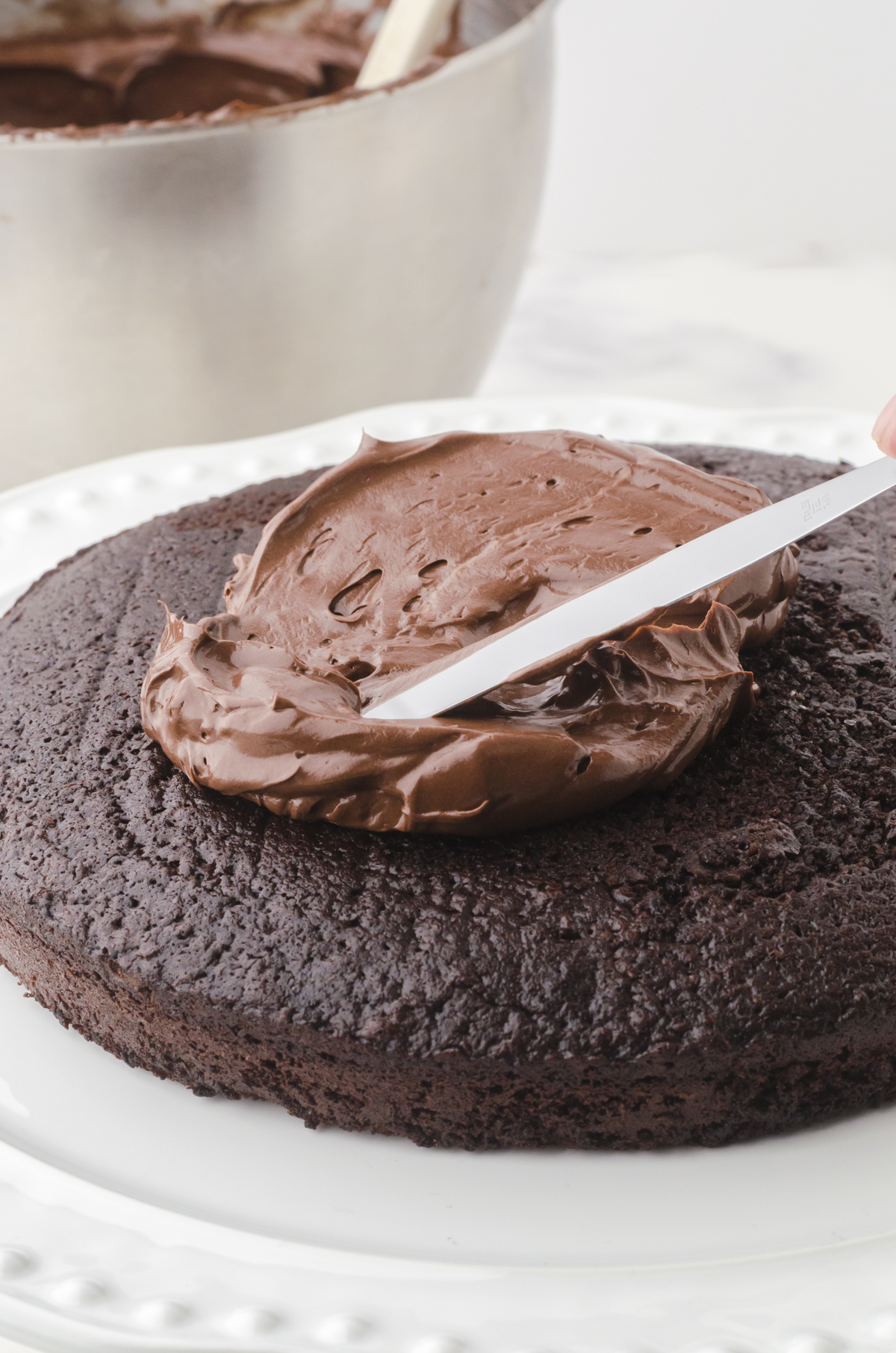 A frozen chocolate cake layer with chocolate frosting being spread on to the top of it.