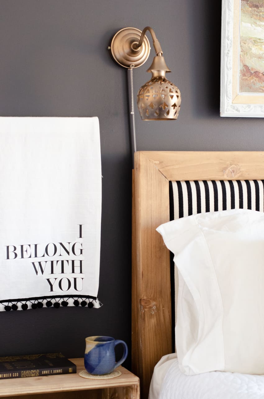 A wall lamp cord cover attached to a wall lamp cord above a headboard.