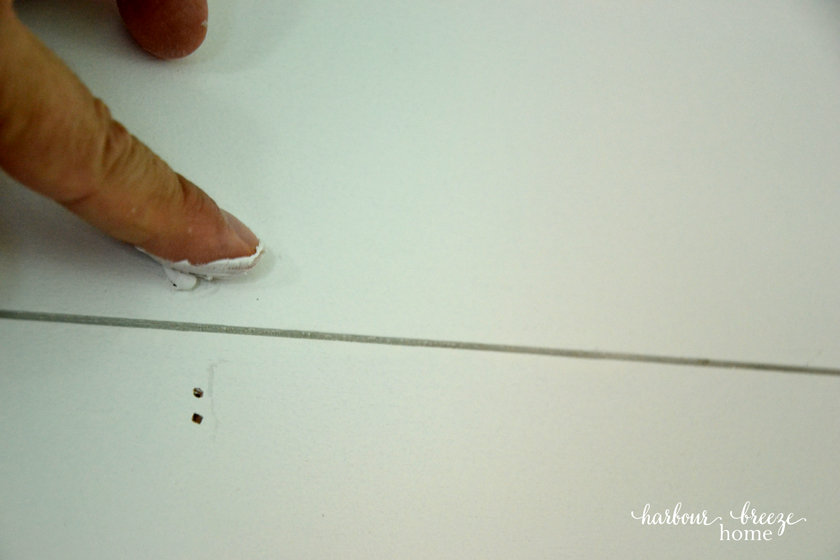 Putting dap on the nail holes with a finger as part of the process of a DIY farmhouse shiplap wall