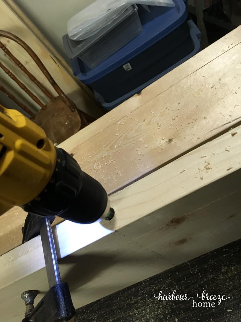 A drill drilling into the DIY floating shelf to make room for the dowel that will be inserted into it.