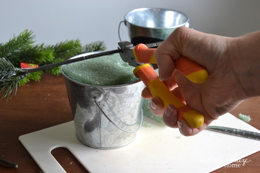 using wire cutters to cut faux branches for a christmas tree mini