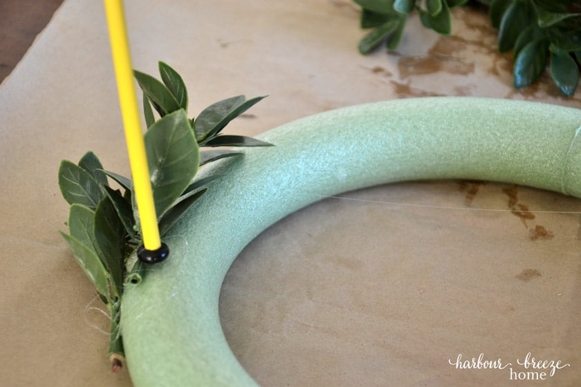 Gluing on faux boxwood leaves to a small foam wreath form
