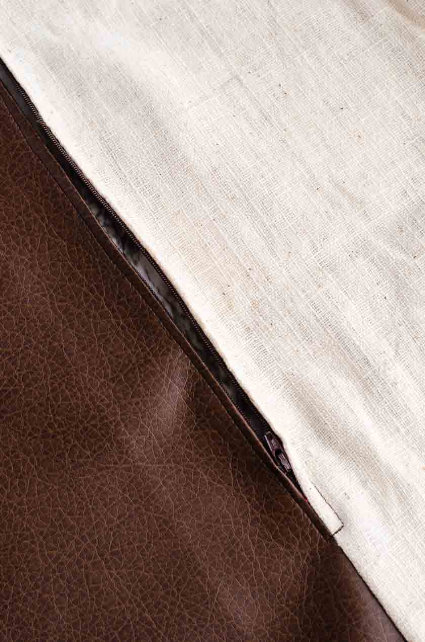 The zipper on the bottom of a faux leather pillow cover with linen back.