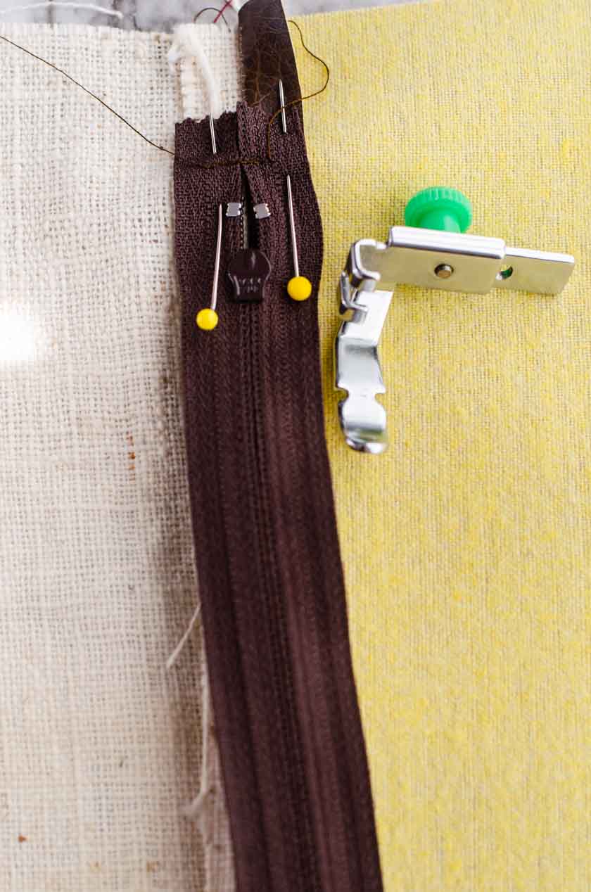 A zipper sewing machine foot beside the pinned in place and ready to sew when making zippered pillow covers.