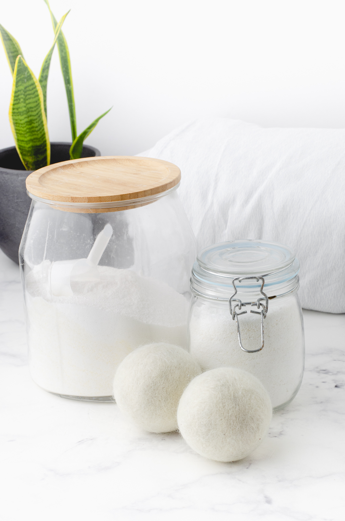 Large glass jar with laundry detergent powder and two wool dryer balls beside it.
