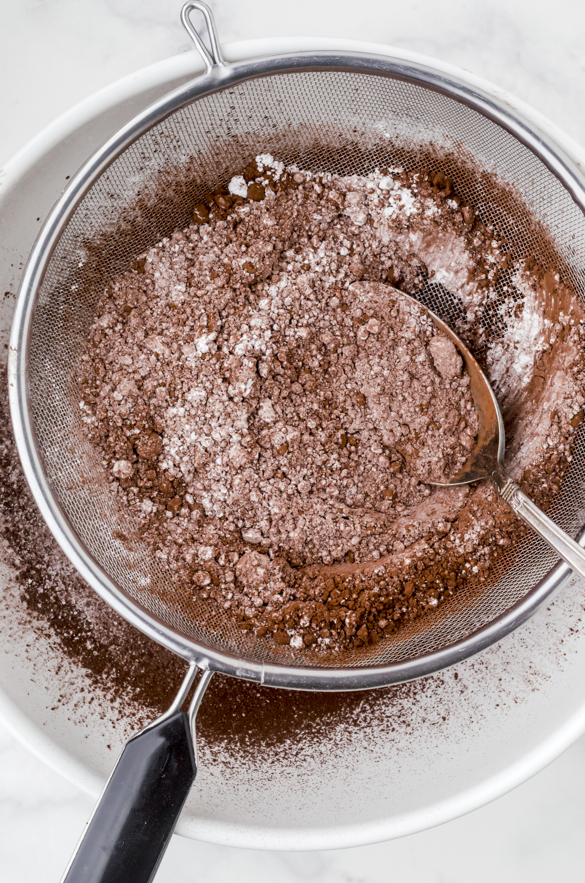Cocoa powder and flour in a fine mesh strainer over a big white bowl