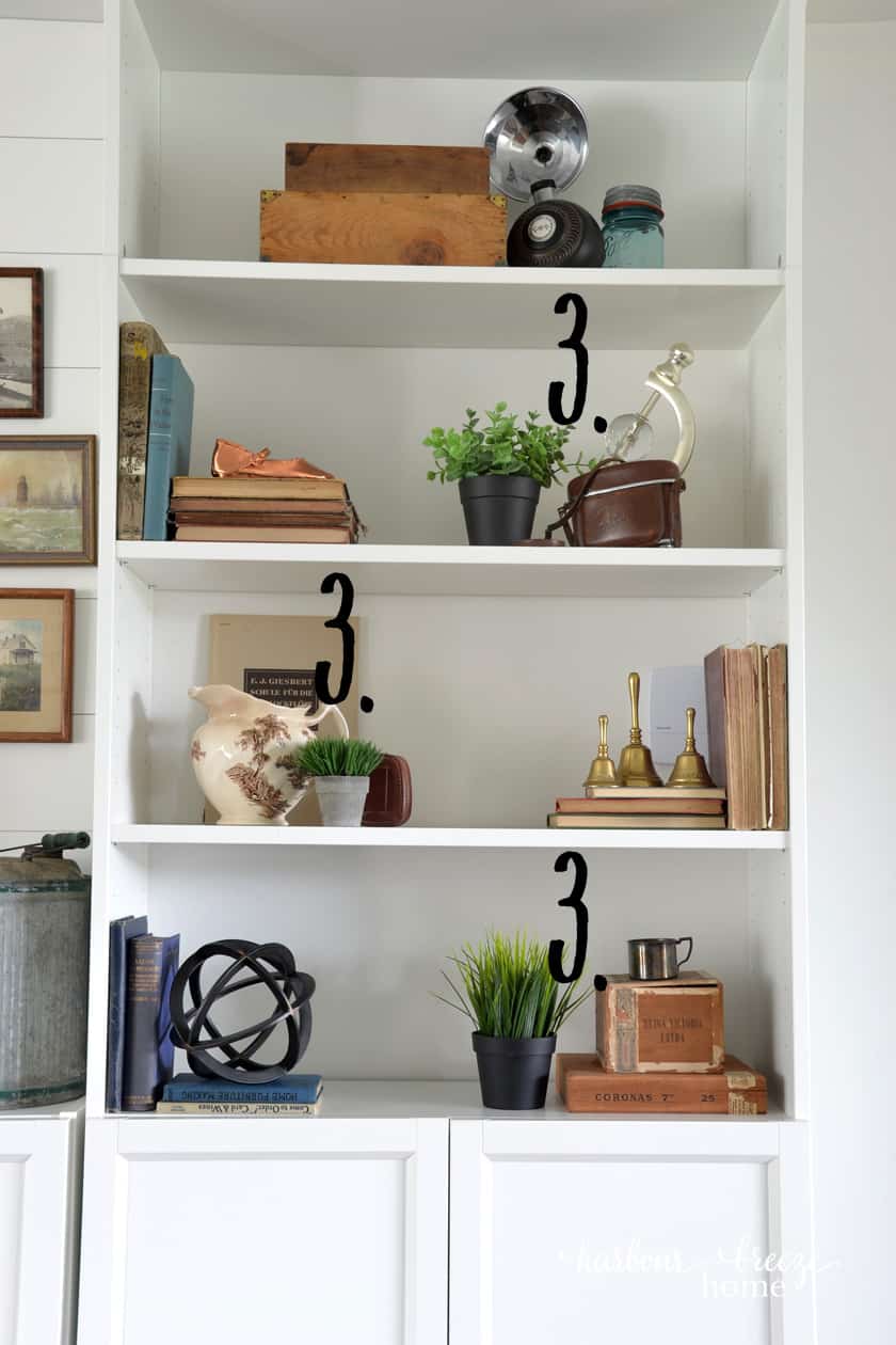 Faux greenery in a variety of pots staggered on shelves of an Ikea Billy Bookcase to add to farmhouse bookshelf decor