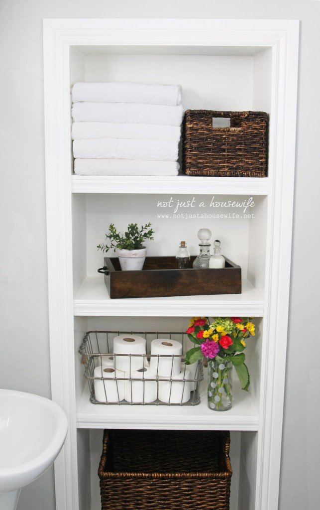 A bathroom design inspired by Joanna gaines and the farmhouse style - with a shelf unit filled with white towels, woven baskets, wooded tray, wire basket, and flowers