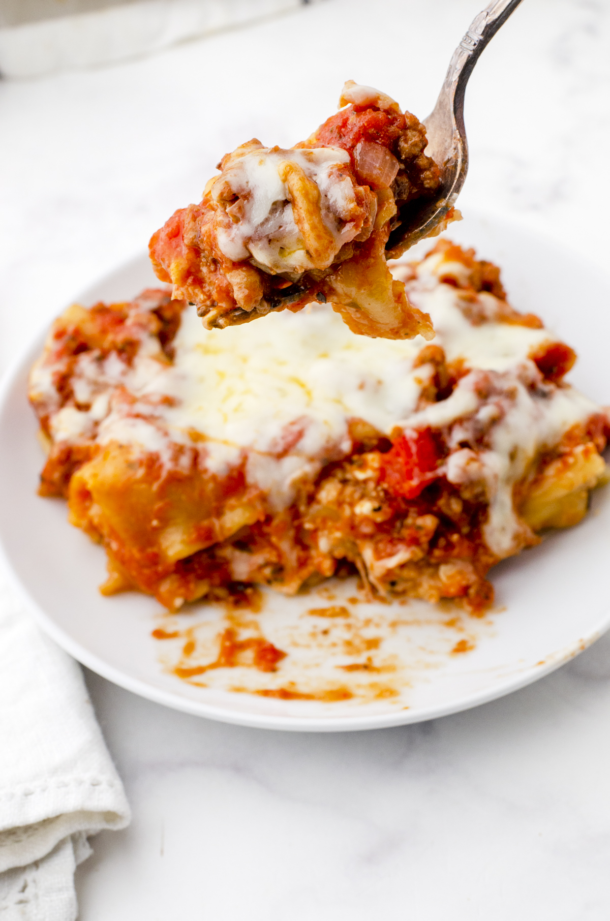 Piece of freeze ahead lasagna cooked and on a dinner plate with a fork holding a bite.