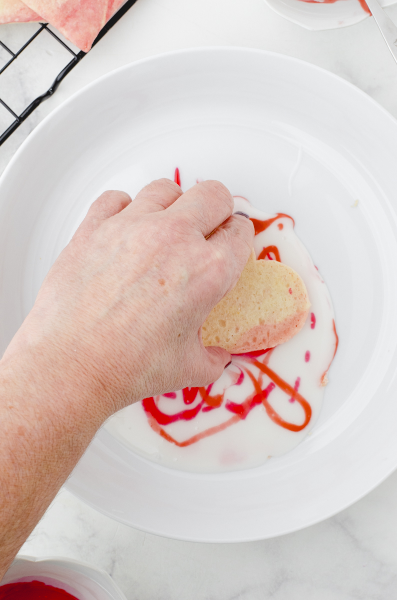 a woman dipping a cookie into the icing with drizzles on it.