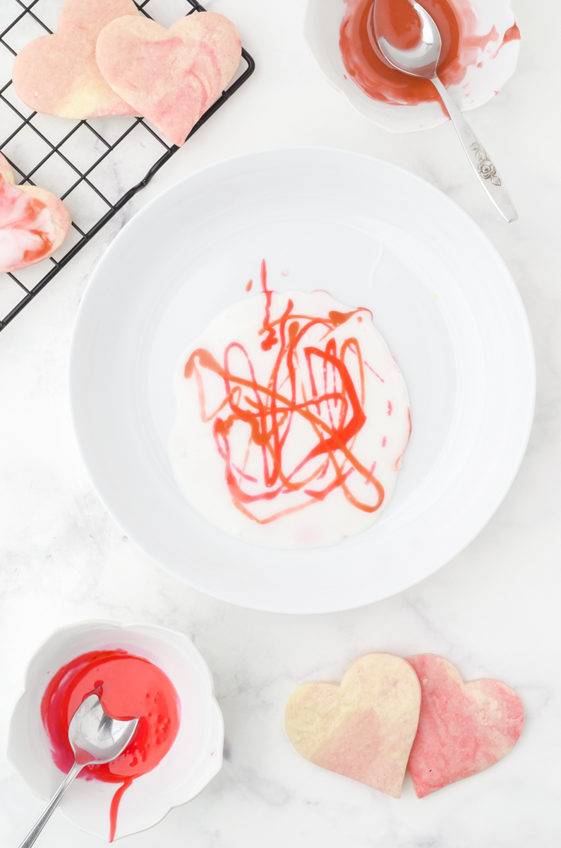 A bowl of white icing with squiggles of the colored icing drizzled randomly on the top.
