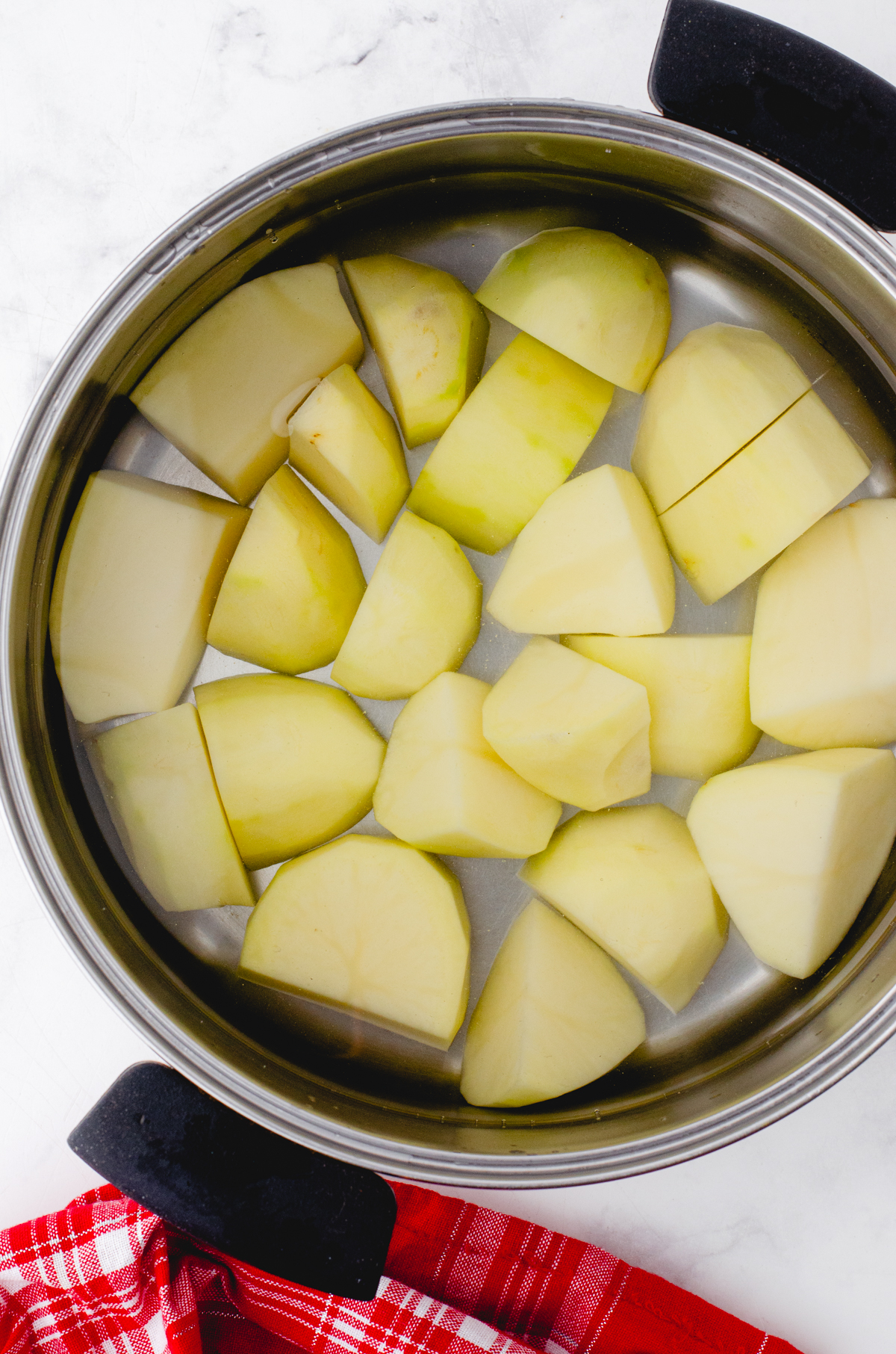 Peeleed potatoes in a pot covered with water.