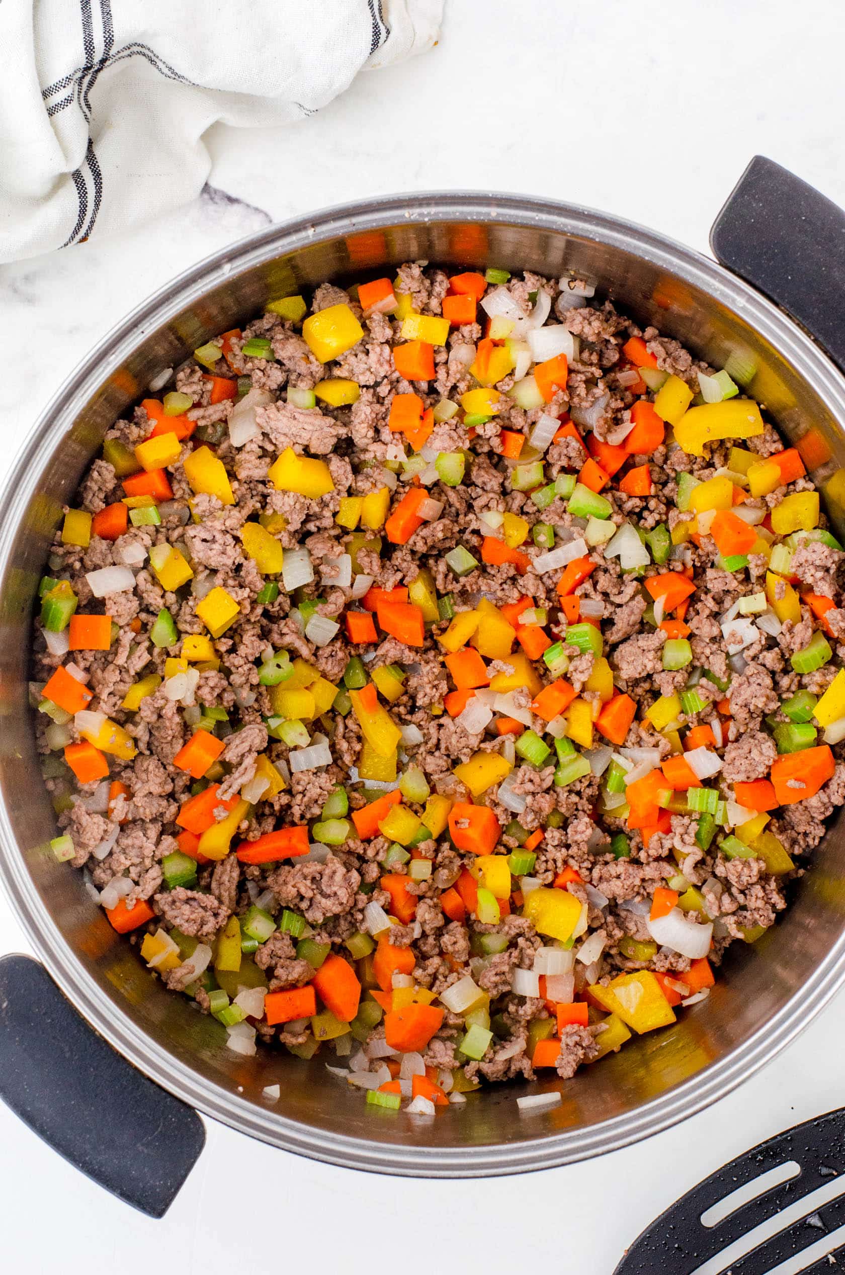 A large stock pot with browned ground beef and veggies as the base for minestrone soup.