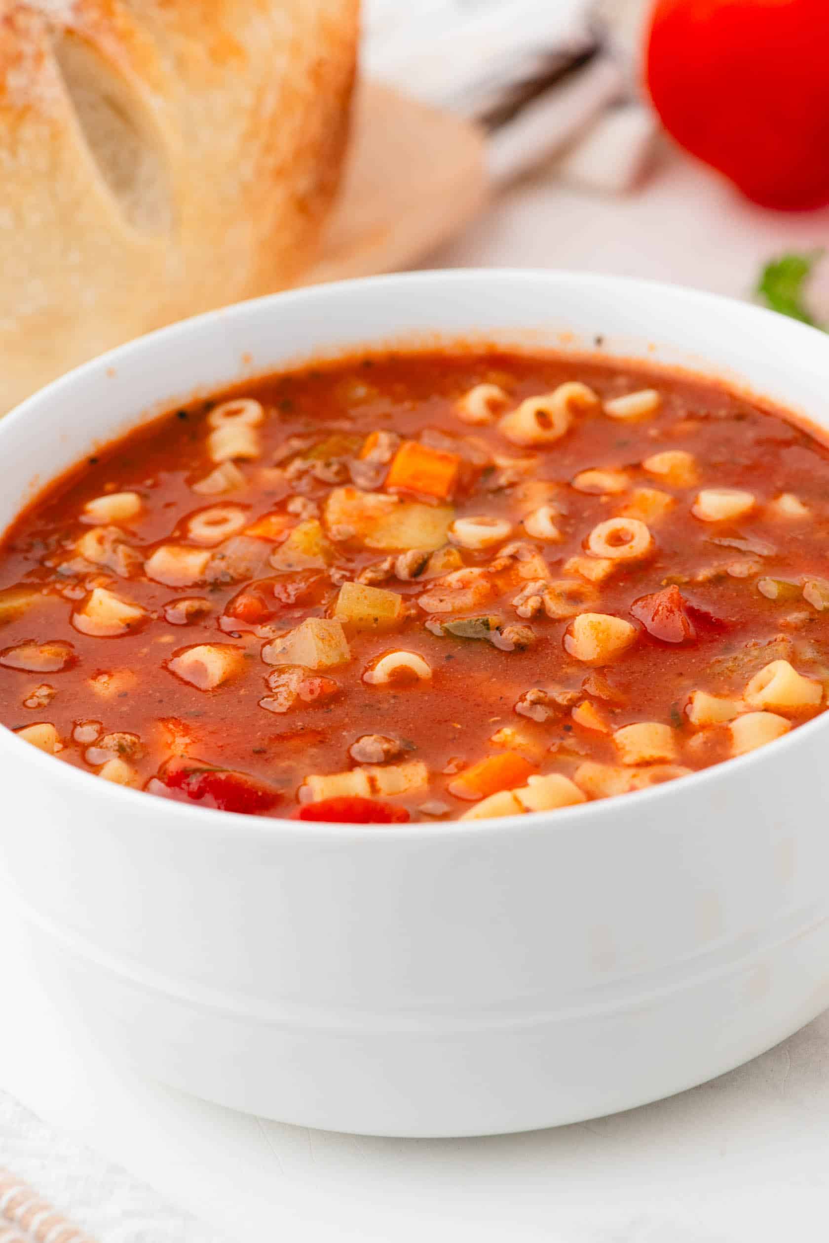 A bowl of Minestrone Italian Soup with fresh sour dough bread behind.