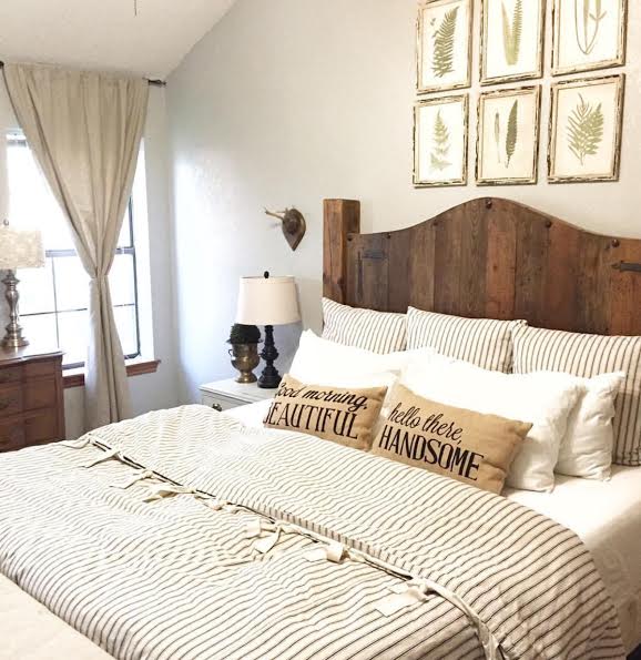 Farmhouse bedroom with a bed with a wooden headboard; botatanical art prints above the bed, and striped linen bedding and pillows.