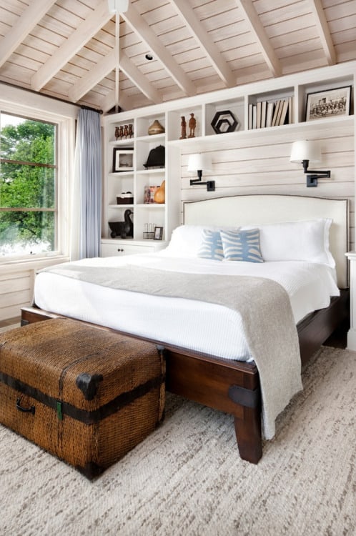 A farmhouse bedroom with a floor to ceiling built in bookcase surrounding the bed with white headboard, wooden fram and white bedding.