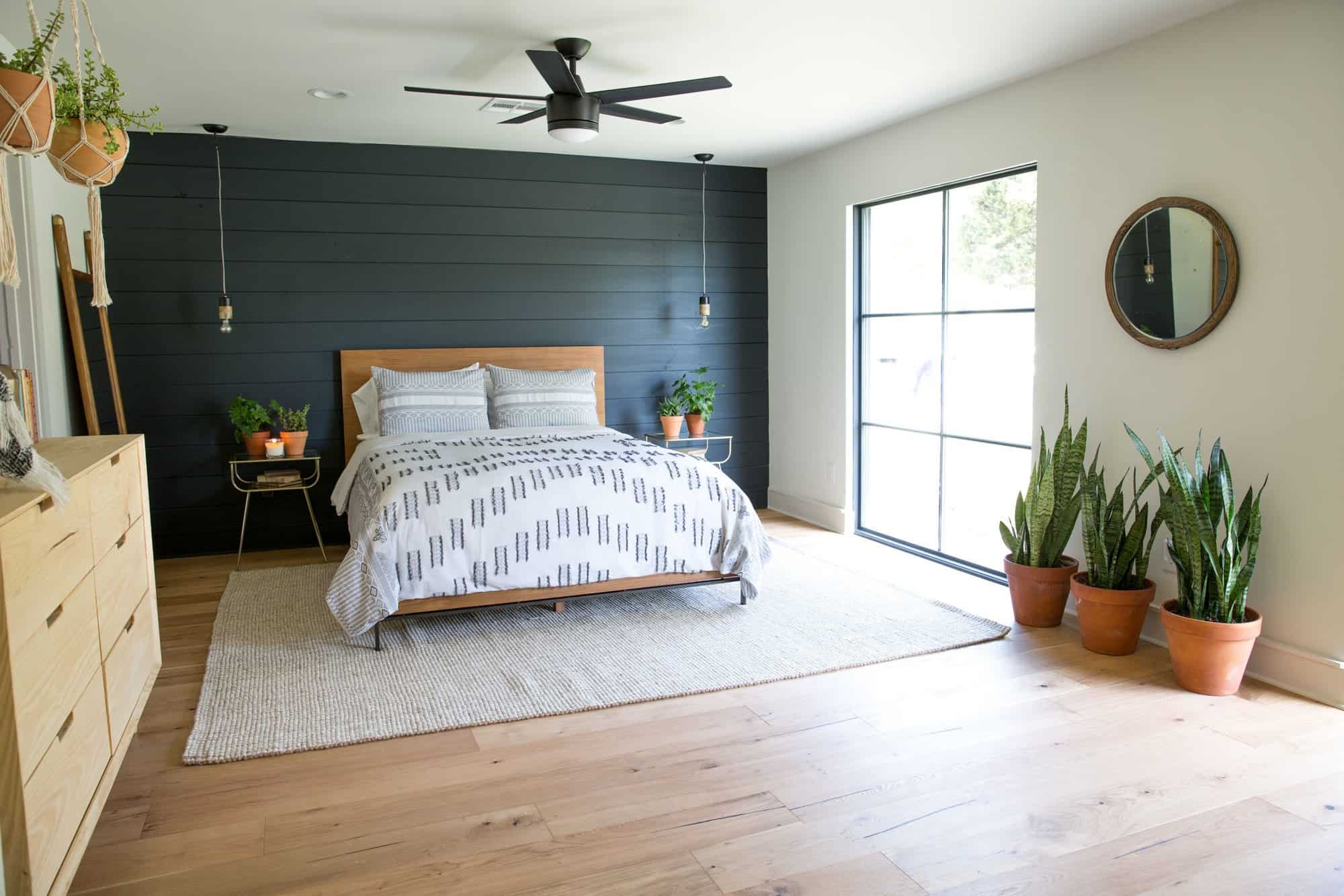 A dark shiplap wall behind a simple medium toned wood headboard