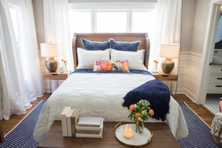 A wooden sleigh style headboard set in front of a big window with nightstands on either side