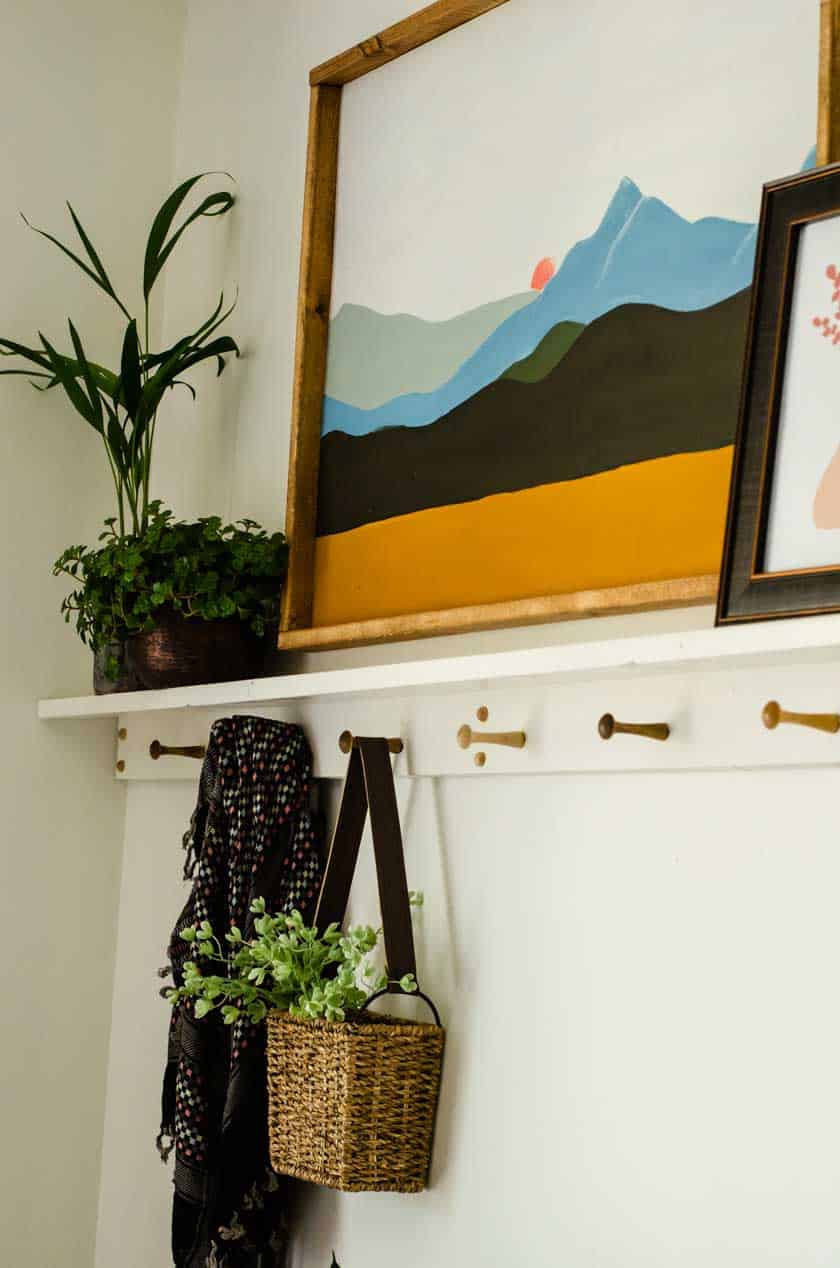 A basket with a handle hanging on one of the pegs of a boho shelf with peg rail underneath.