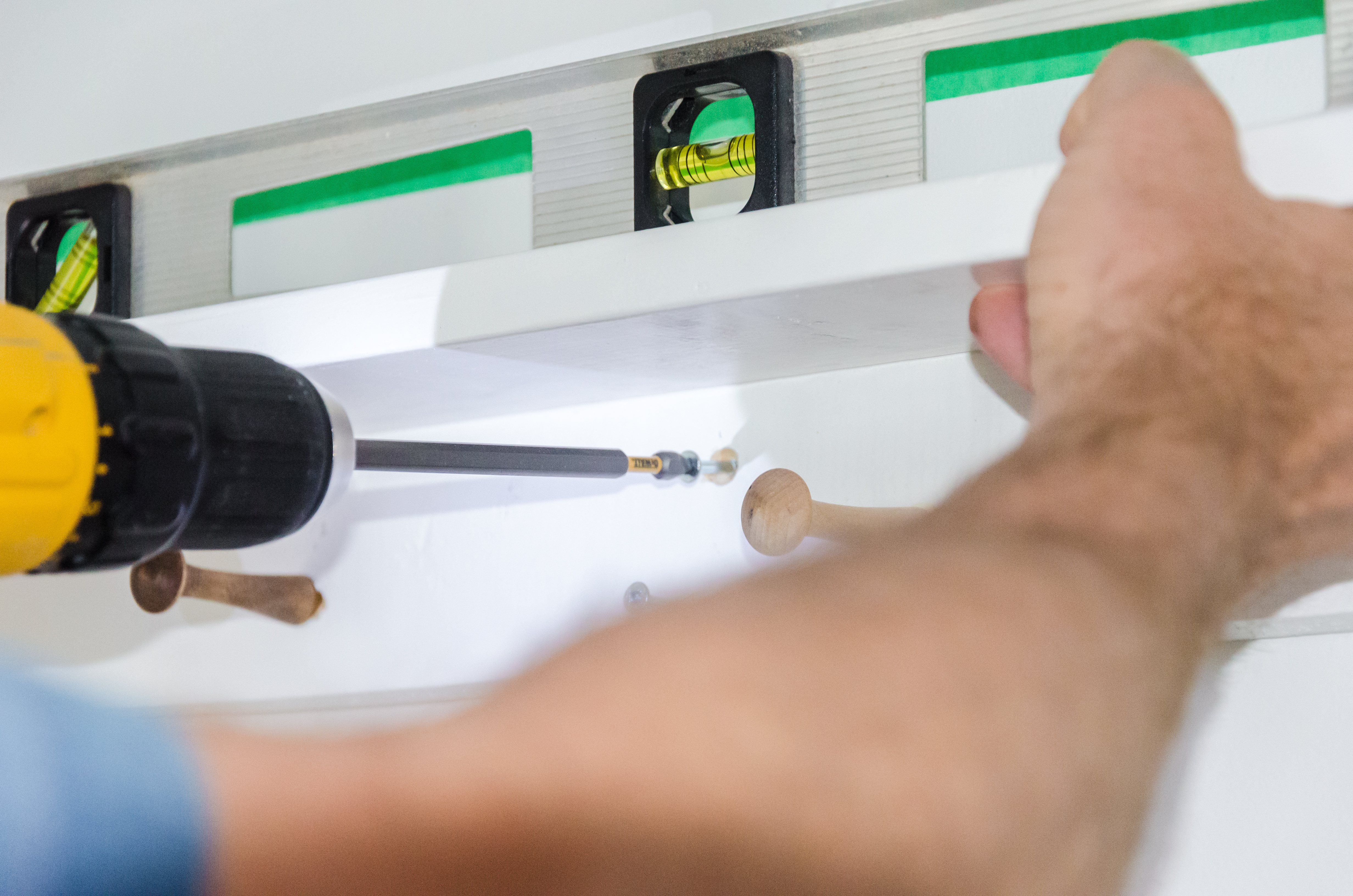 using a drill with a screwdriver attachment to hang a boho shelf on the wall