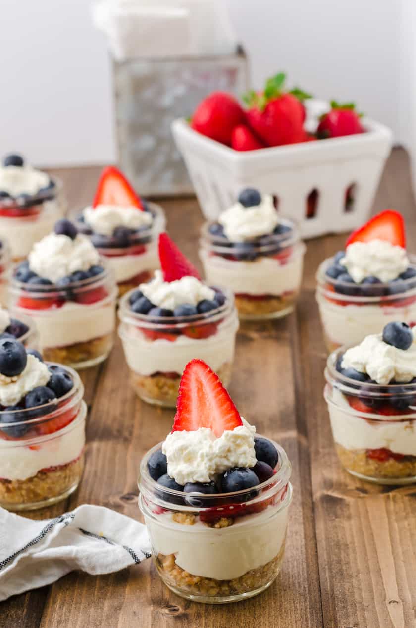 Cheese cake jars sitting on a wooden table with a basket of strawberries behind.