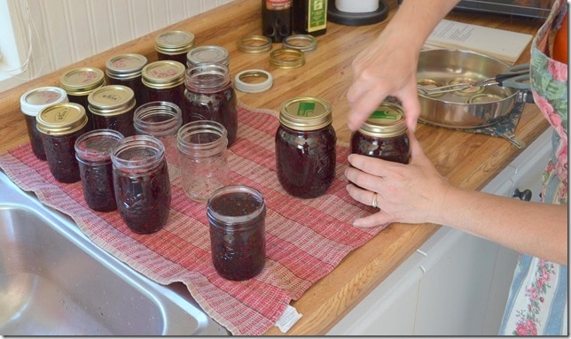 a woman twisting on the lid to a homemade jar of blackberry jam
