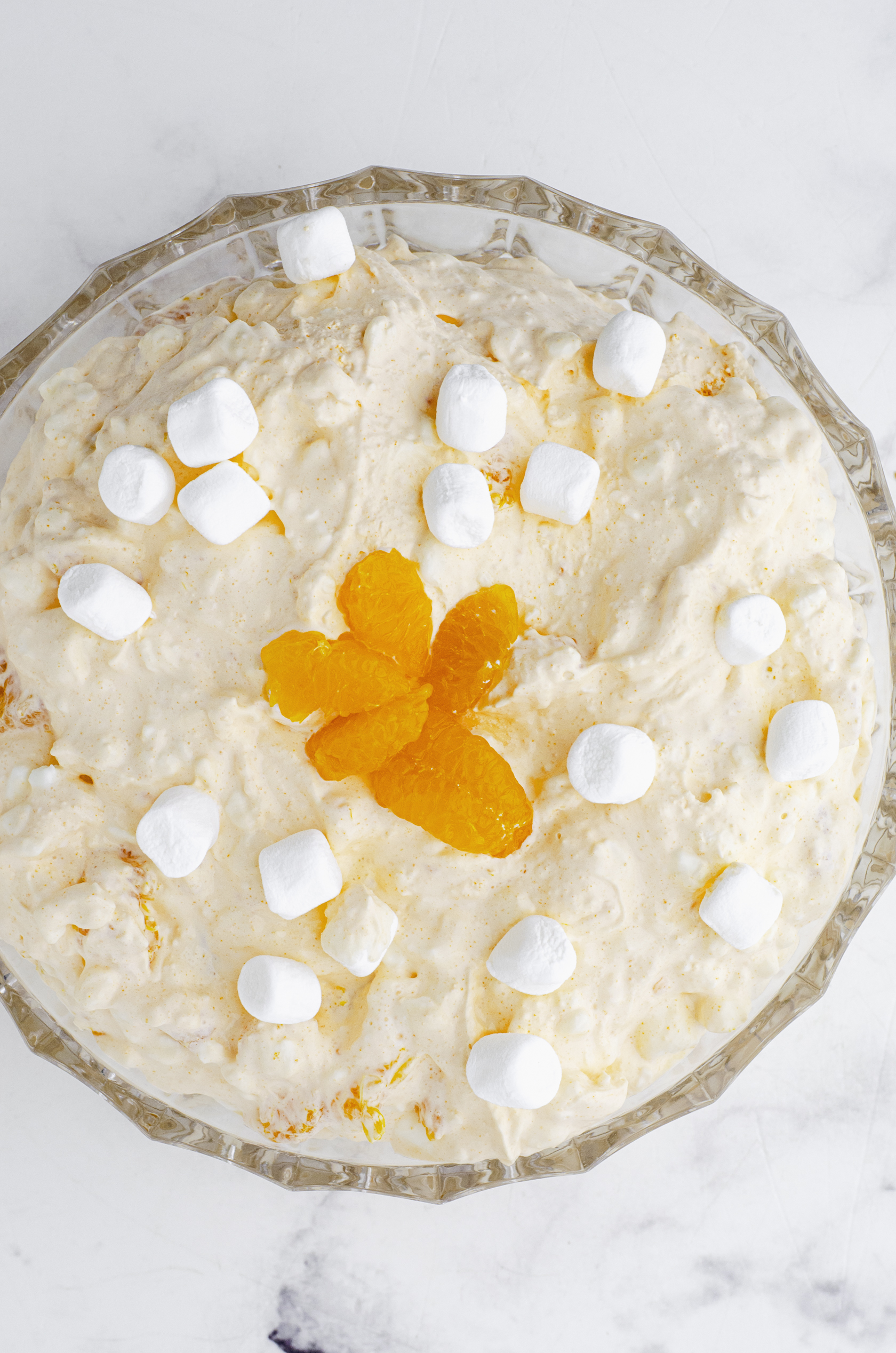 Orange fluff salad in a glass serving bowl with marshmallows and orange slices decorating the top.