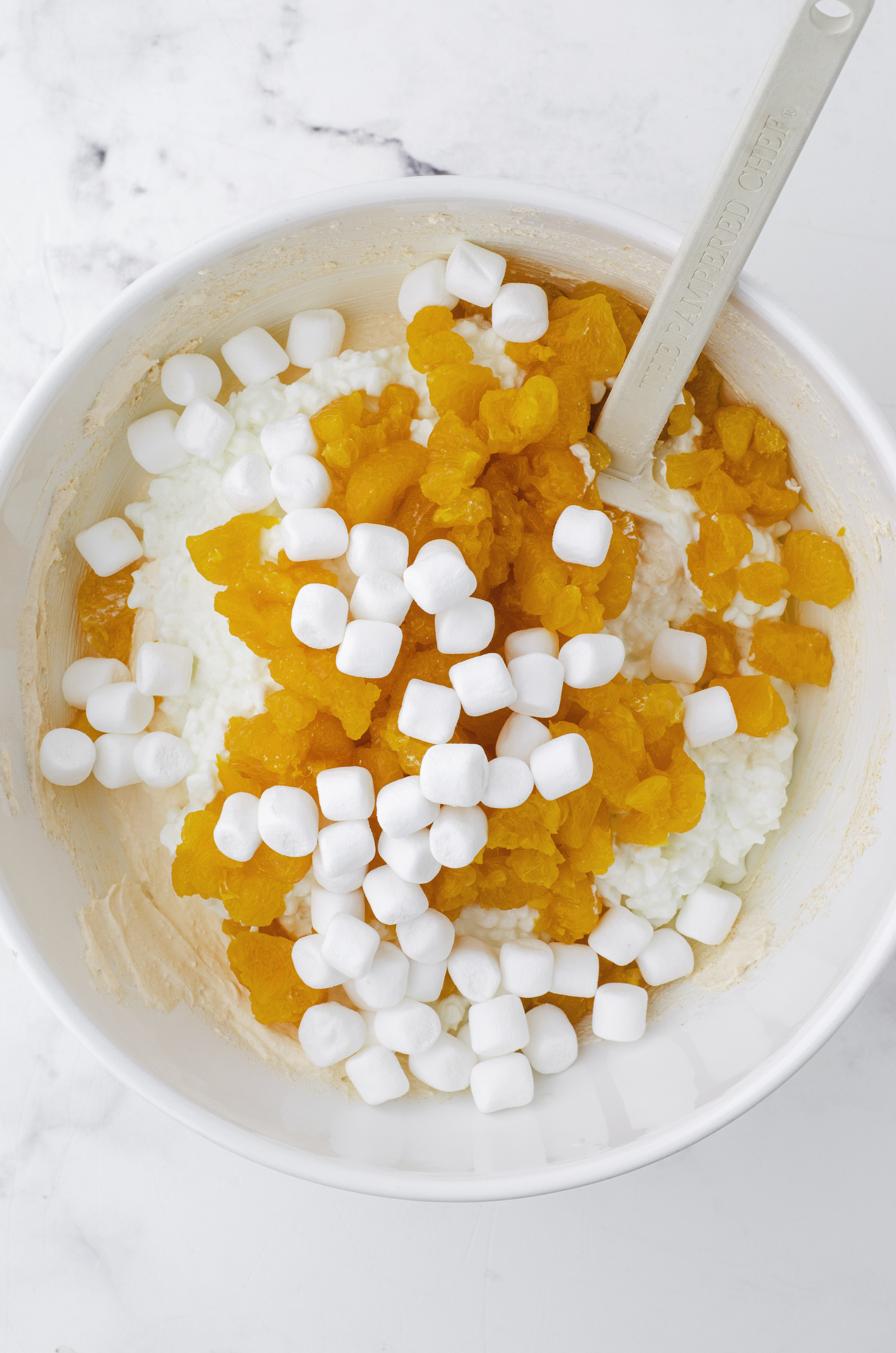 Oranges, marshmallows, and cottage cheese added to the orange jello powder and cool whip mixture in a large bow.