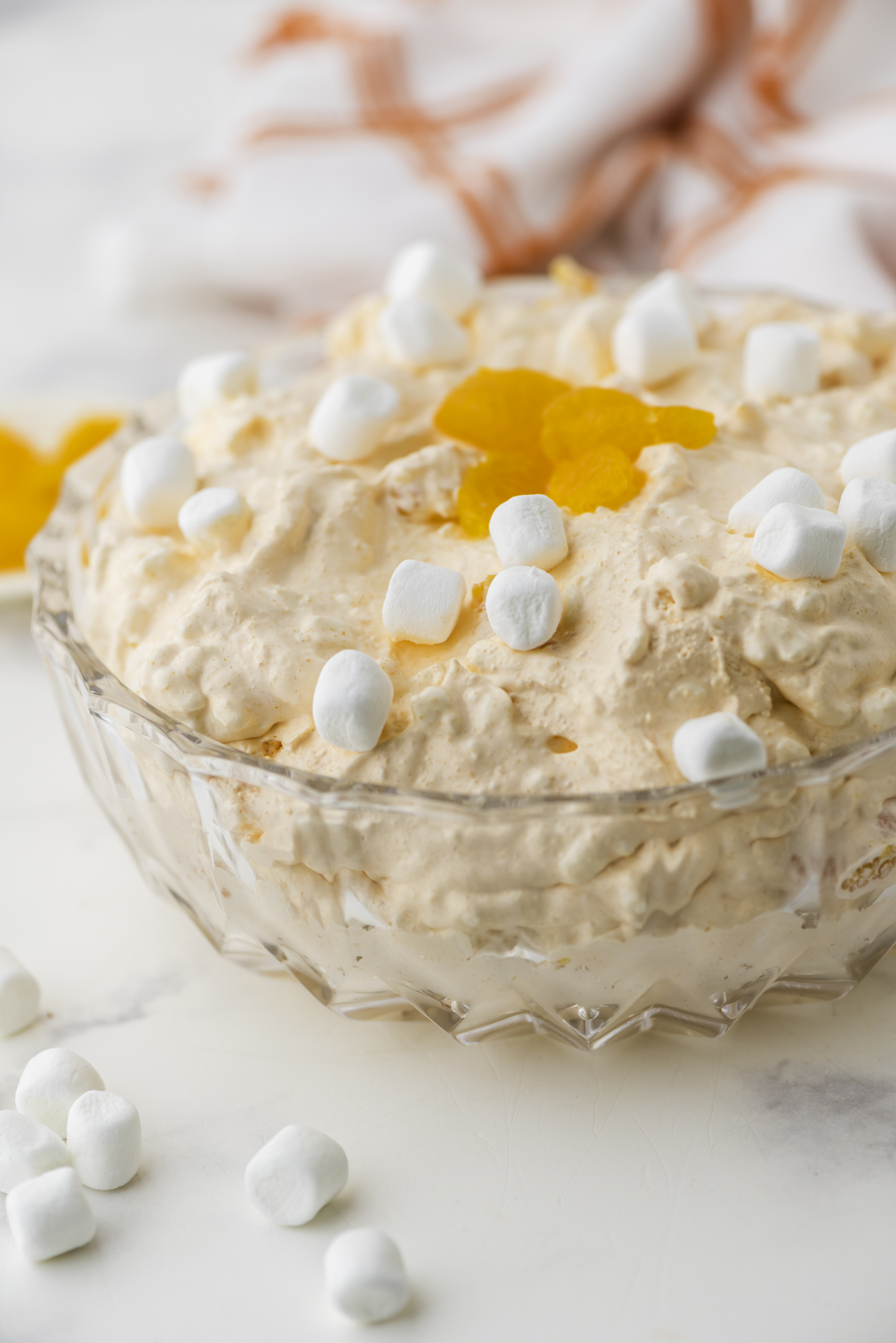 Classic orange fluff salad in a clear glass serving bowl with marshmallows and mandarin oranges garnishing the top.