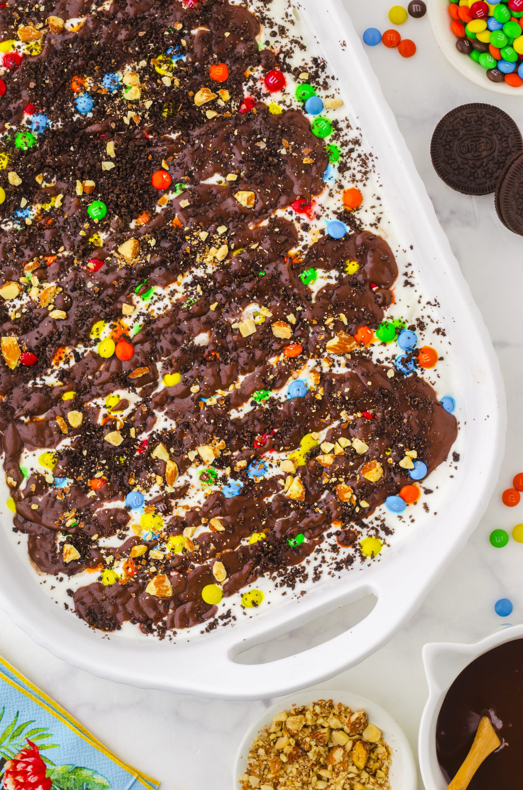 9x13 pan of ice cream cake with oreos, vanilla ice cream, hot fudge sauce and m&ms