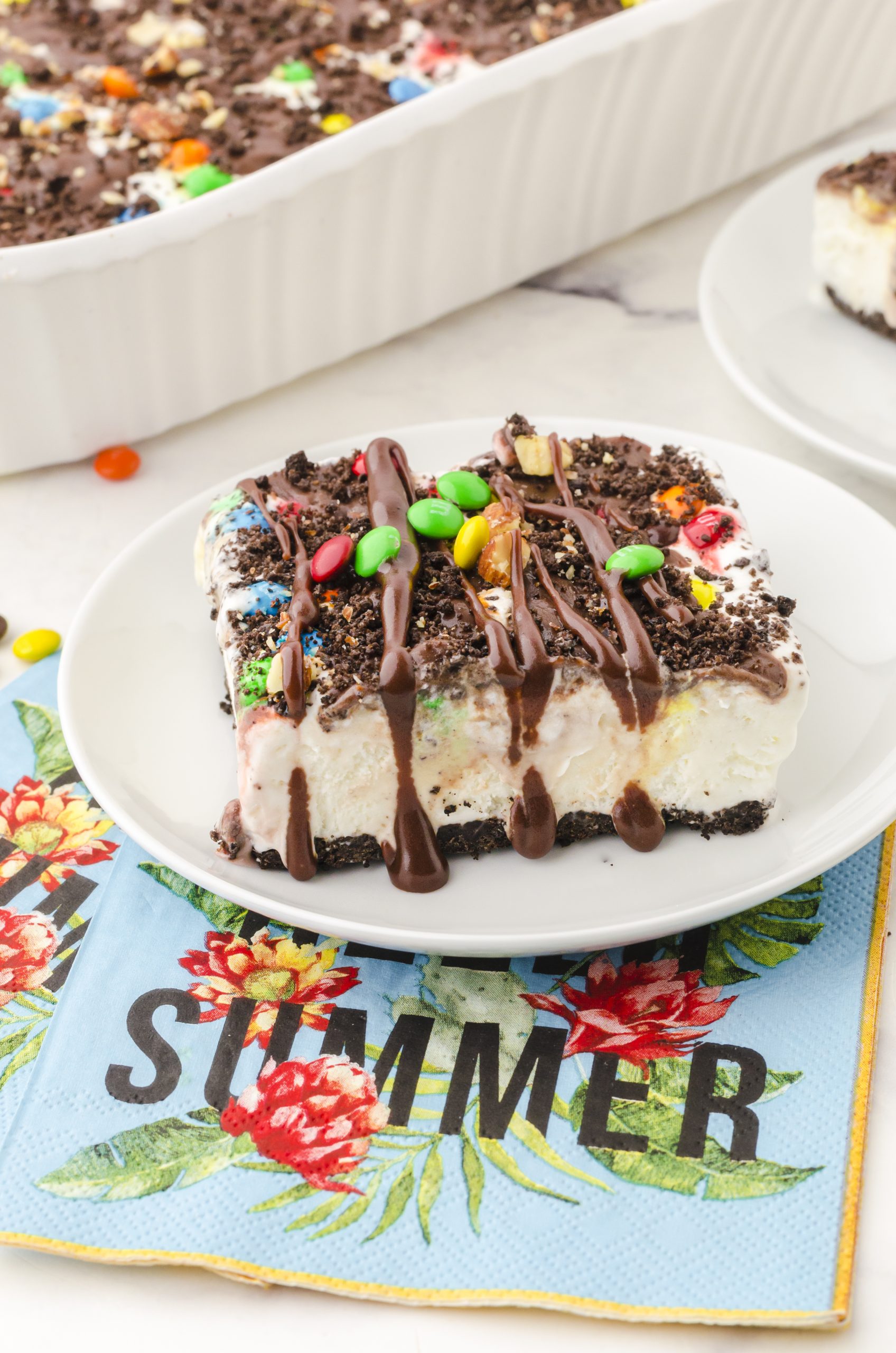 Oreo ice cream cake on a dessert plate drizzled with hot fudge sauce and a sprinkle of m&ms on the top