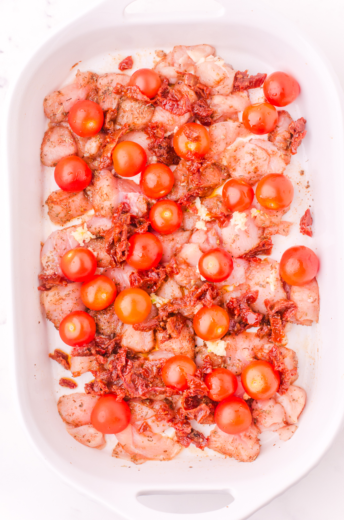 Cherry tomatoes and sundried tomatoes scattered over the top of diced chicken in the baking dish.