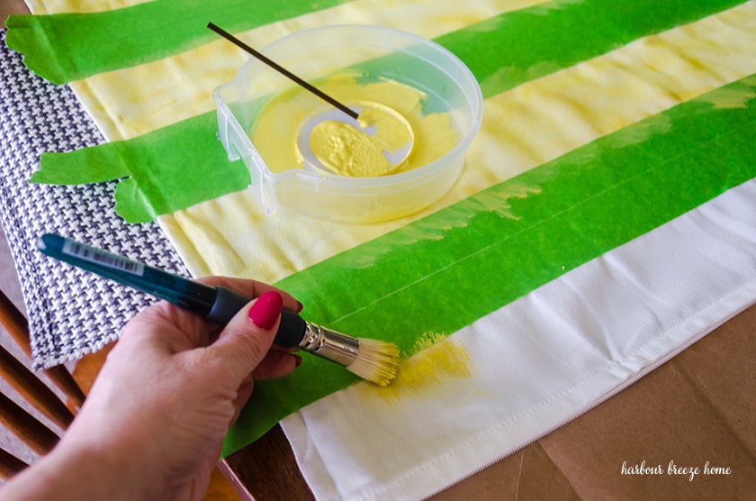 Painters tape on a fabric pillow cover and paint being applied so that stripes will form.