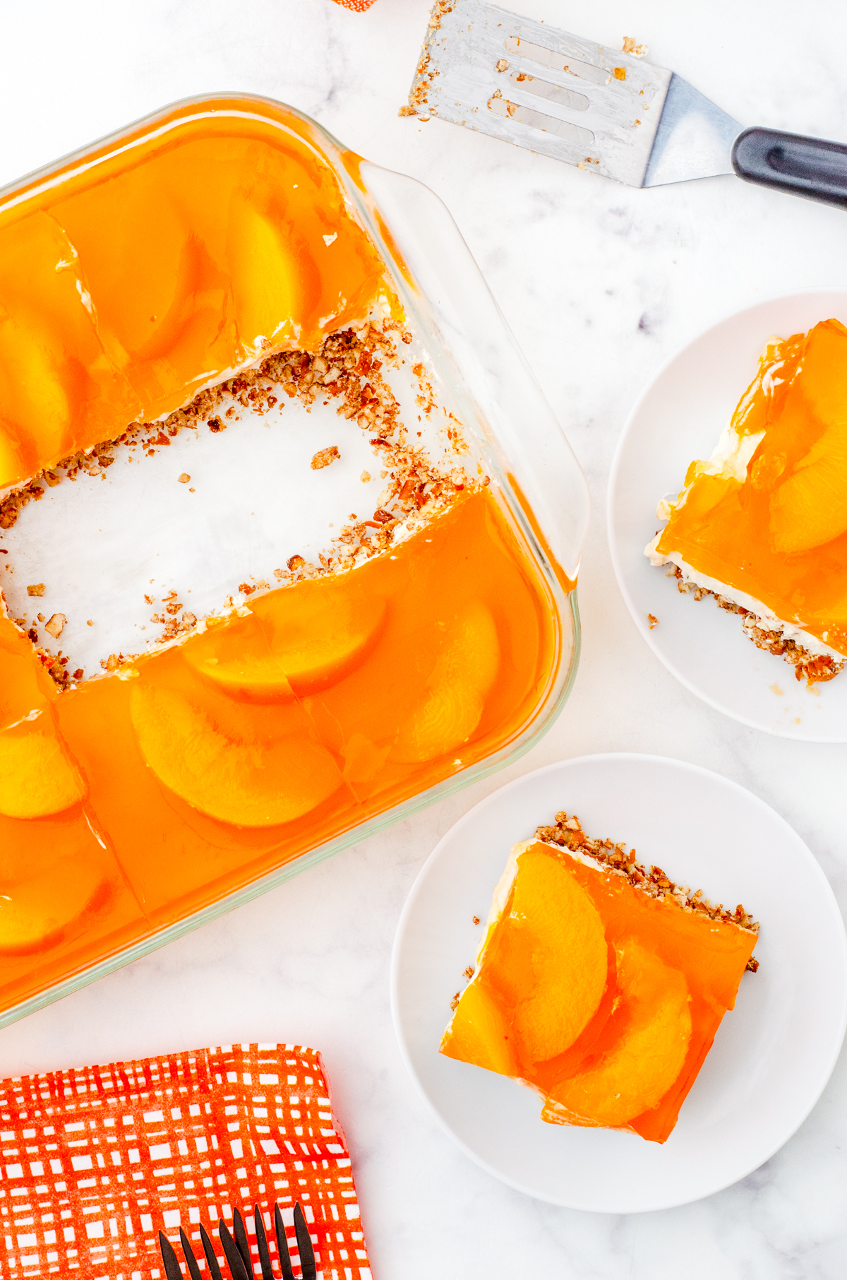 A pan of peach pretzel salad with two pieces cut out and on dessert plates.
