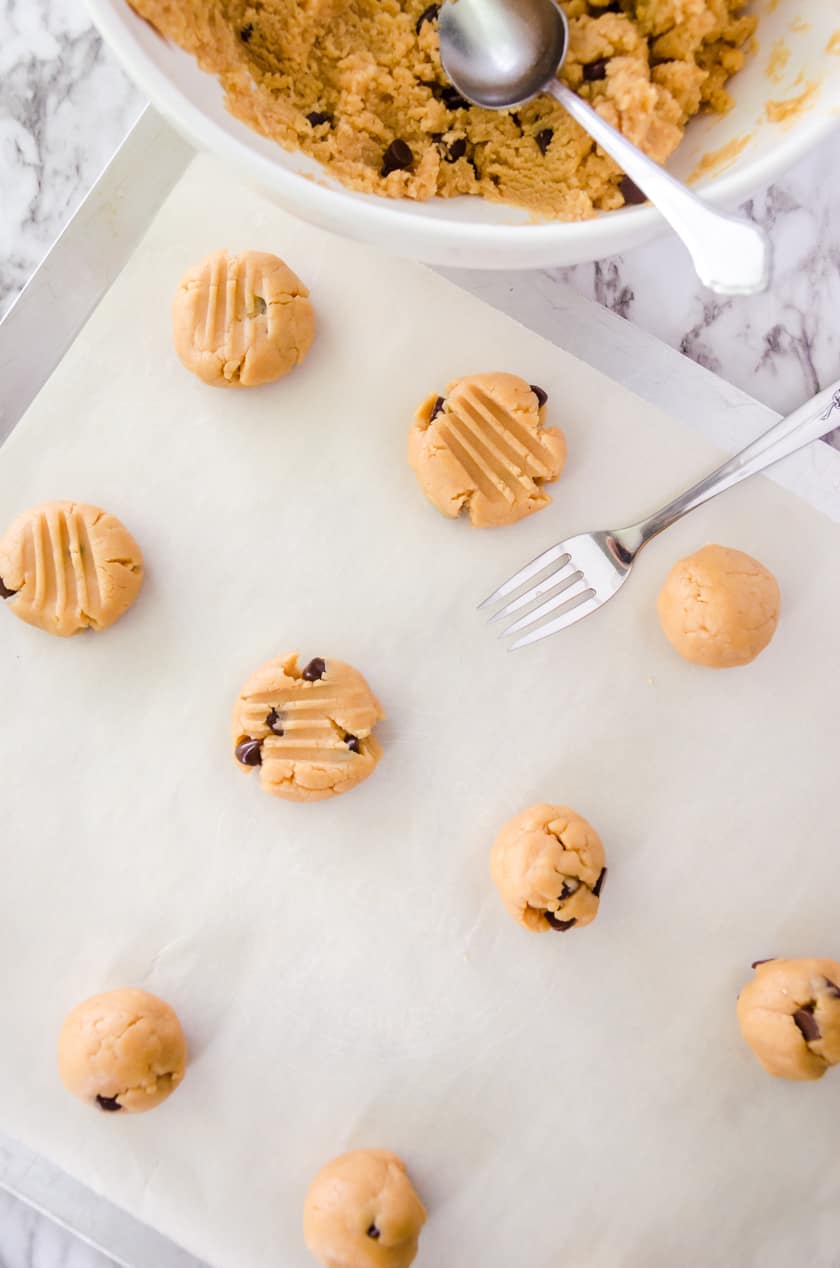 Peanut butter chocolate chip cookies being flattened before baking on a cookie sheet.