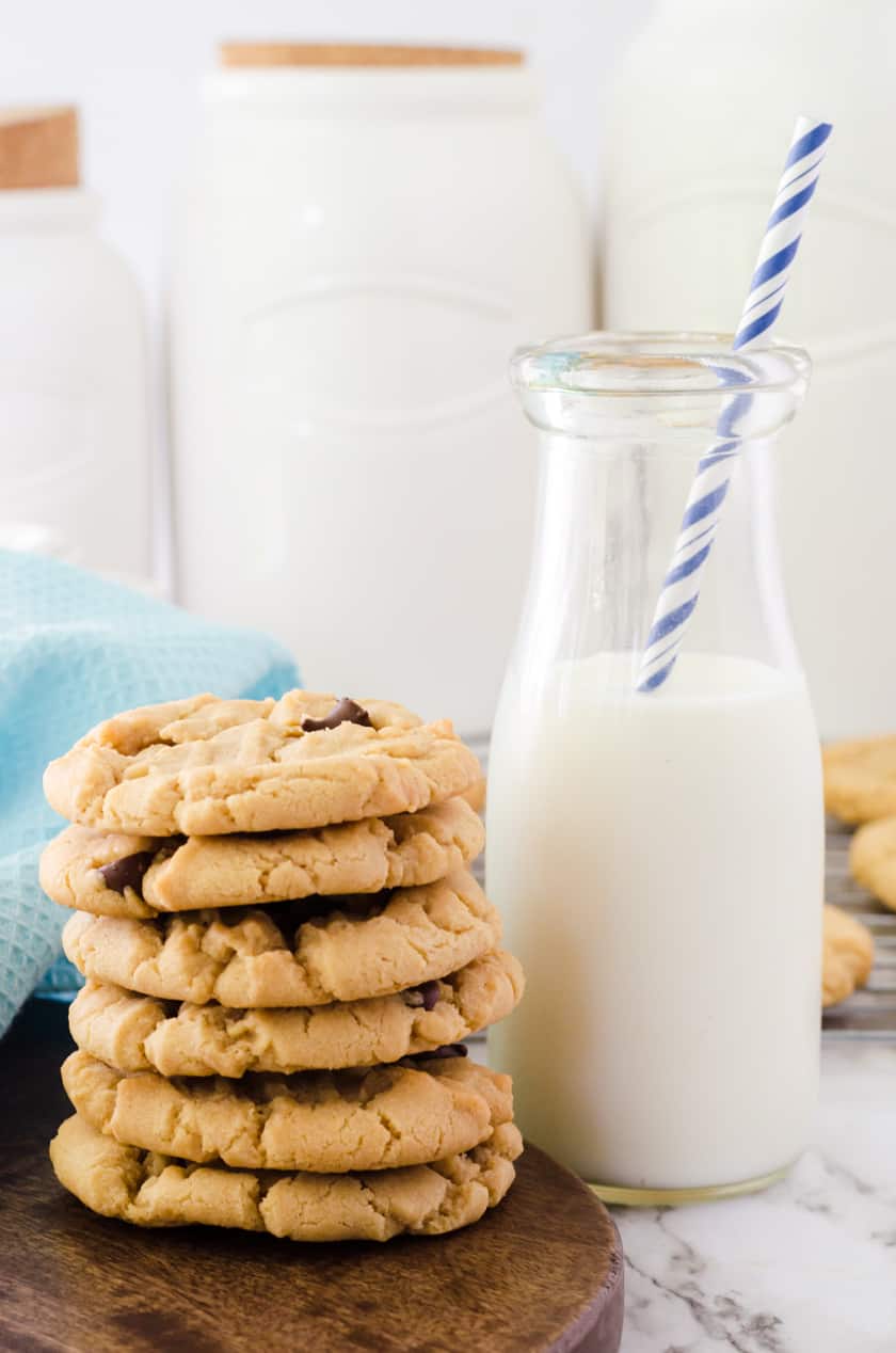 a stack of peanut butter chocolate chip cookies beside a cup of milk