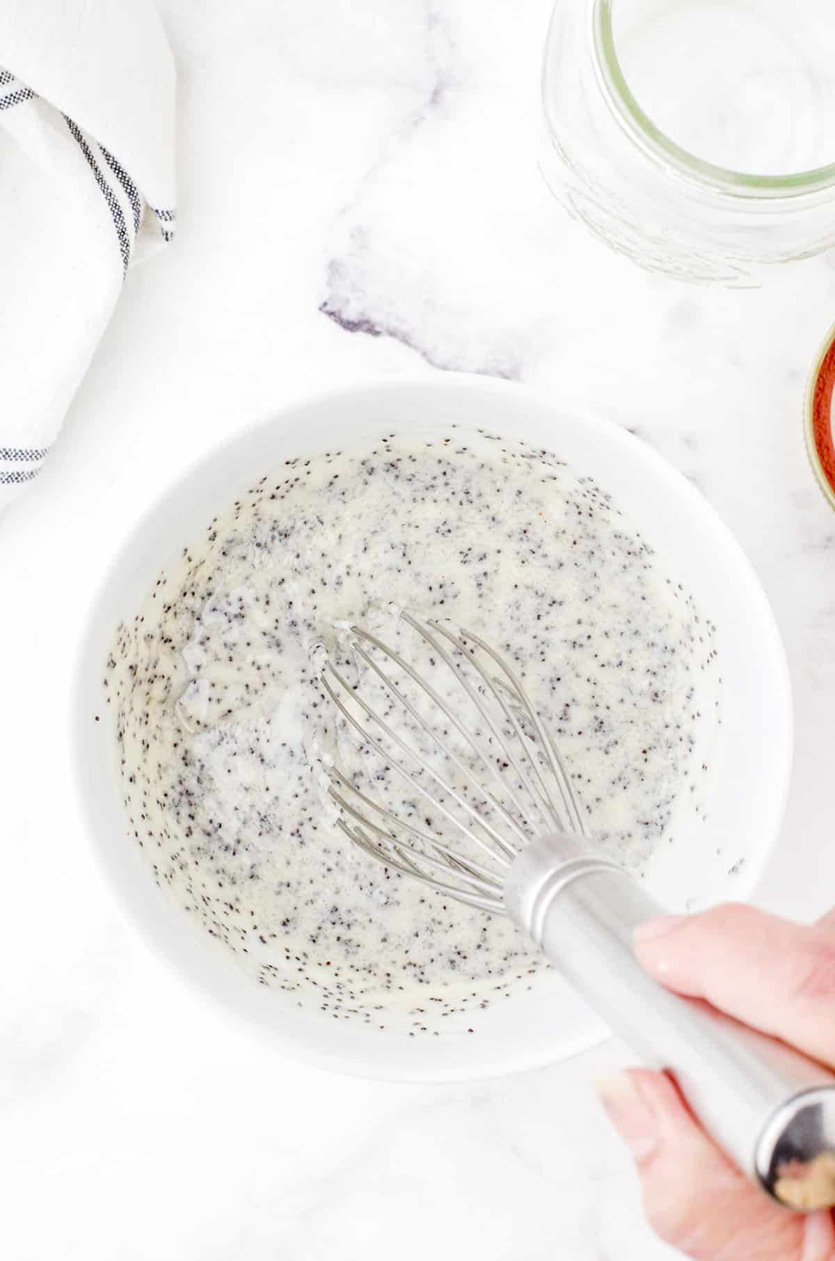 Creamy poppyseed dressing being mixed together with a whisk in a medium sized bowl.