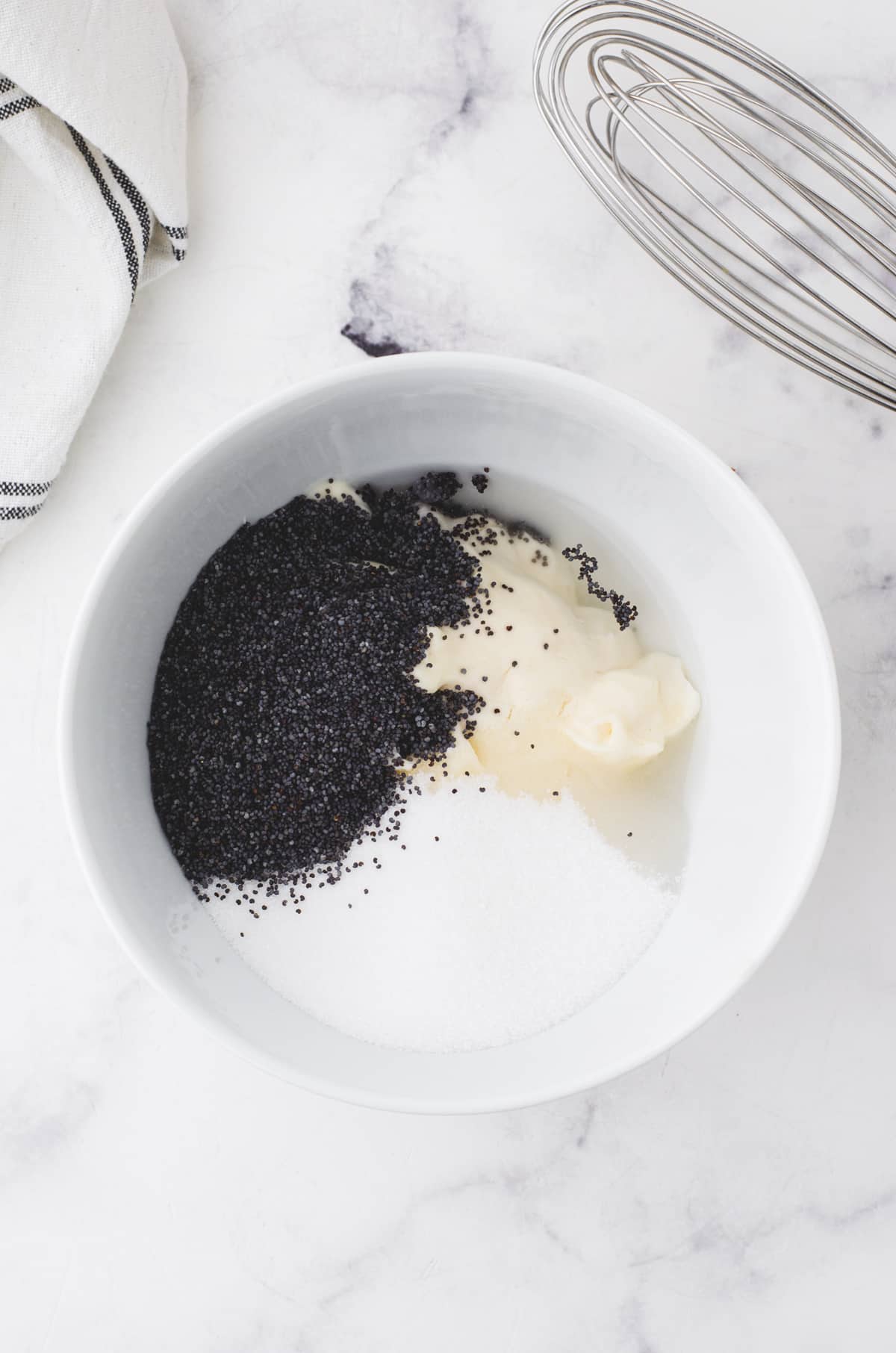 Ingredients for creamy poppyseed dressing in a bowl with a whisk beside it.