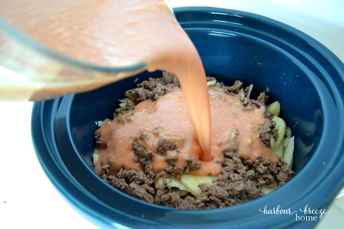 liquid being poured over the layers of ingredients in the crock pot