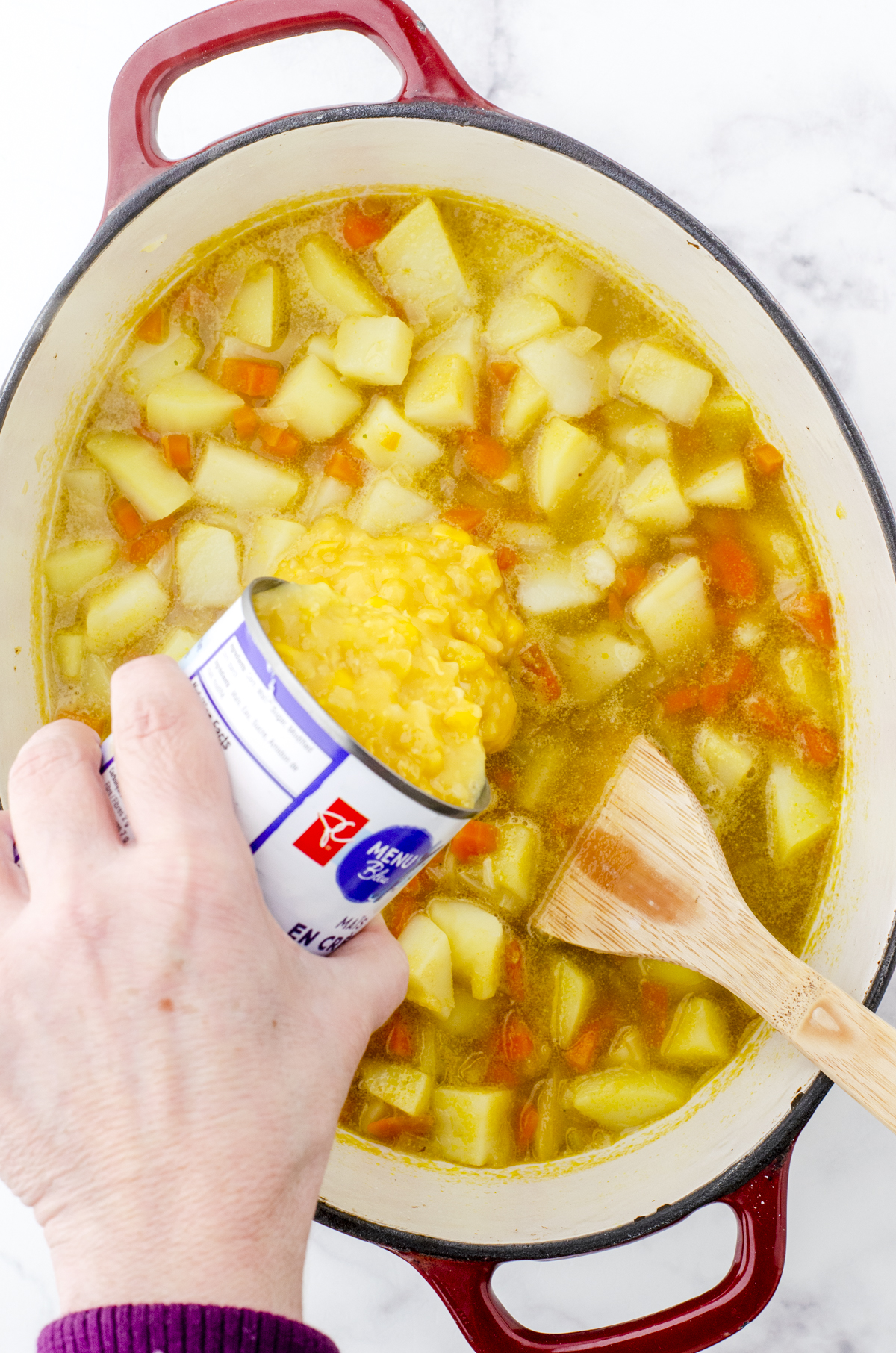 Creamed corn being added to the pot of potato soup.