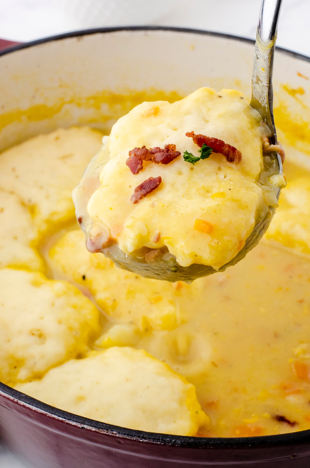 A ladle with potato soup with a drop dumpling on the top.